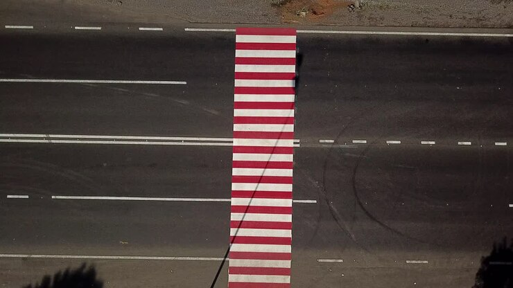 Truck is passing through the crossing with red and white stripes painted on black asphalt. Top view of crosswalk for pedestrians in the road at daytime. Aerial view