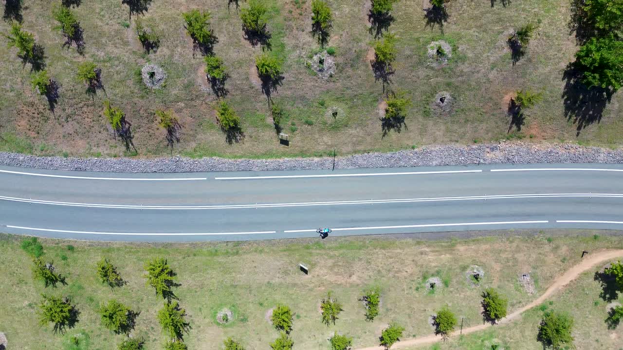 Drone aerial landscape of bicycle rider cycling uphill slope in valley on main road street surrounded by trees nature Botanical Gardens National Arboretum park Canberra ACT Australia sports leisure