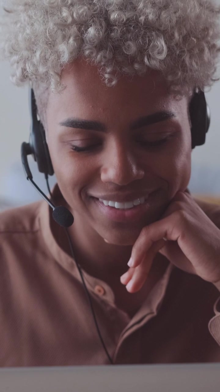 Agente di supporto afroamericana sorridente che parla con le cuffie nel suo ufficio domestico