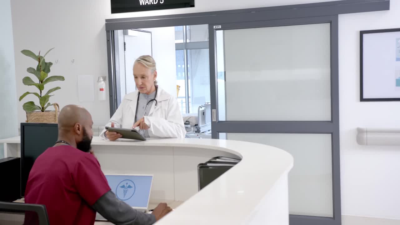 Diversi medici, uomini e donne, in discussione che usano un tablet nella reception dell'ospedale, al rallentatore.