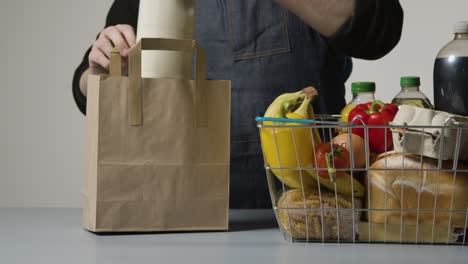 foto de estudio de un trabajador de la tienda empacando alimentos básicos en una cesta de compras de alambre de supermercado en una bolsa de papel 2