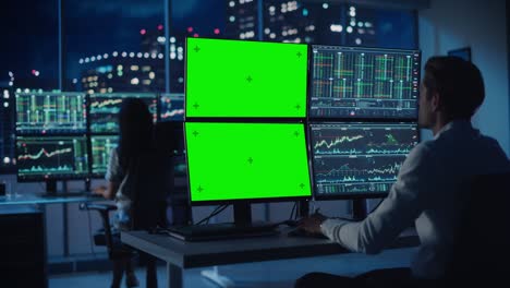 analista financiero que trabaja en una computadora con estación de trabajo multi-monitor con pantalla verde chroma key mock up plantilla y gráficos de acciones en tiempo real. hombre de negocios trabaja en un banco de inversión tarde en la noche.