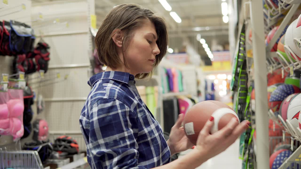 mujer joven seleccionando equipos deportivos en el supermercado. escogiendo una pelota para el fútbol o el fútbol