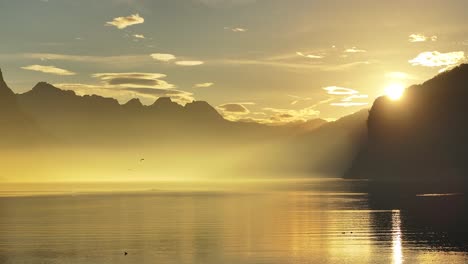 sunrise light pierces through misty mountains over the calm walensee lake with a golden reflection
