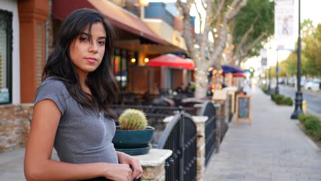 a beautiful hispanic woman standing on the downtown urban city street full of shops, restaurants and retail stores slow motion