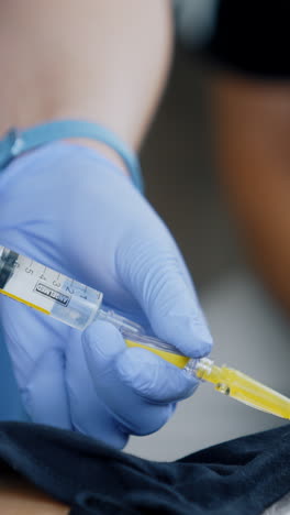 hands in latex blue gloves holding a syringe. giving injection to a patient. close up. vertical video