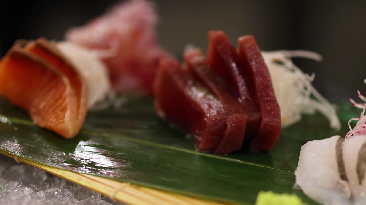 A detailed view of salmon and tuna sashimi arranged on a bamboo leaf with wasabi garnish.
