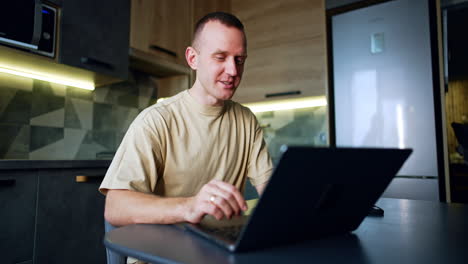 happy relaxed smiling man sits looking at laptop. freelancer working in his kitchen. low angle view.