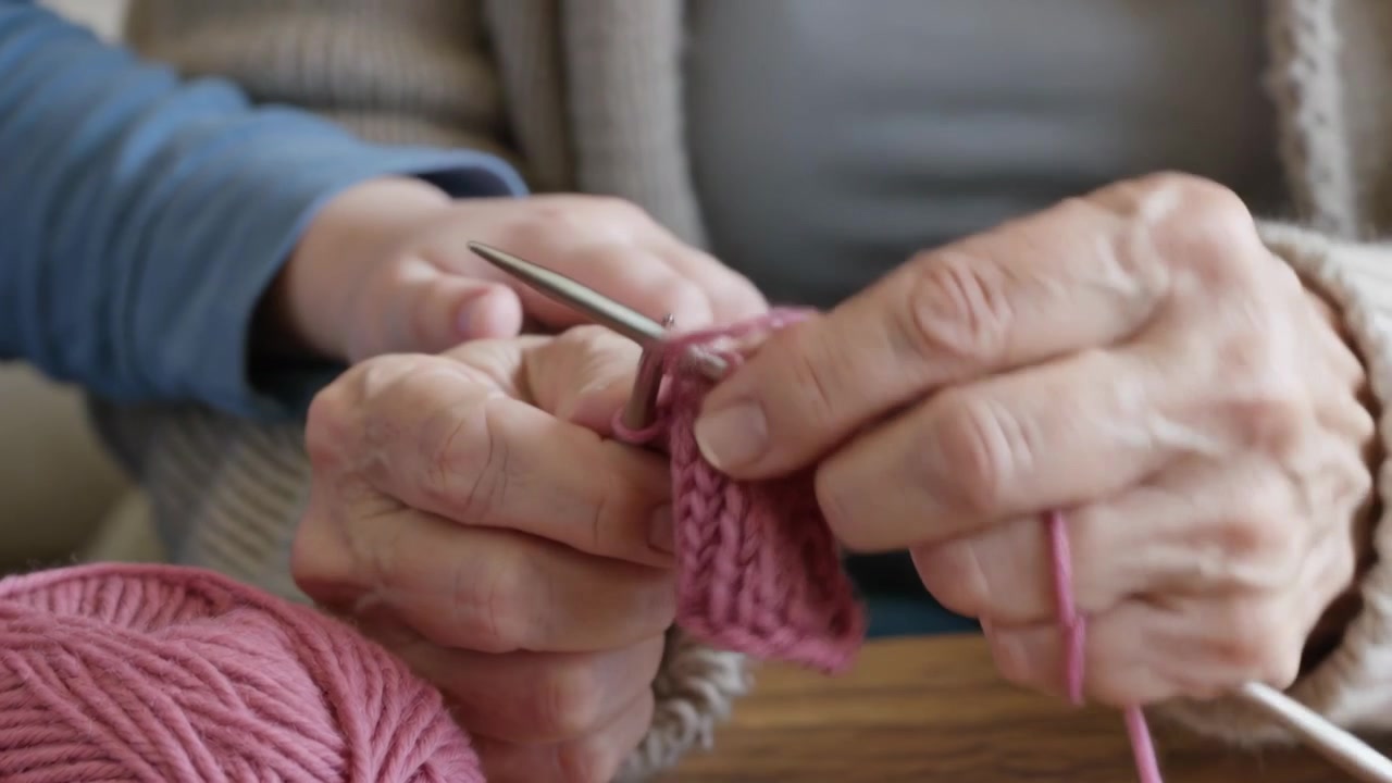 Teaching helper touching hands knitter in cardigan inserting metal needle pulling pink yarn at home