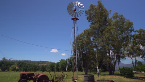 pan down of a rustic windmill beside a vintage tractor and wine barrel flower planters on a farm in northern california