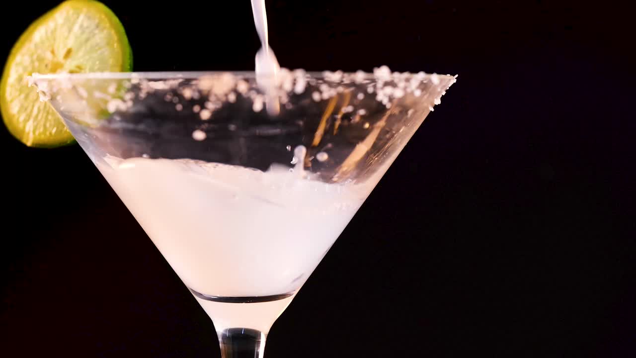 vertiendo margarita en un vaso con guarnición de lima