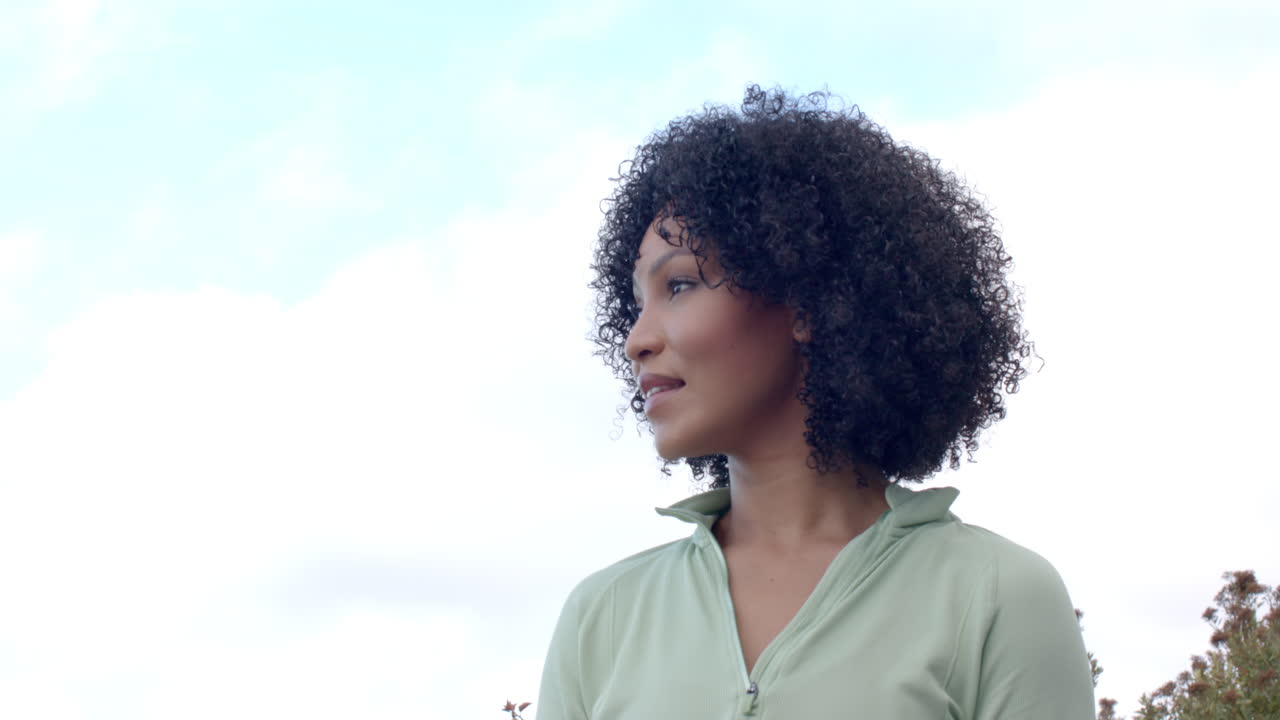 Biracial woman with curly hair smiling outdoors, copy space