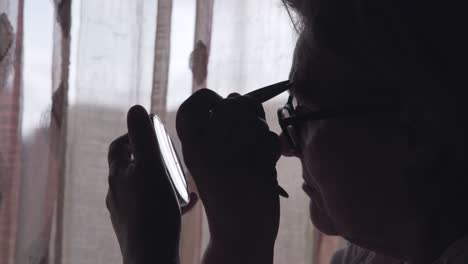 woman applying makeup by window