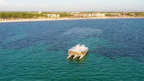 Trimaran-party-boat-stationed-near-resort-beach-at-Punta-Cana-Dominican-Republic,-Aerial-orbit-left-shot