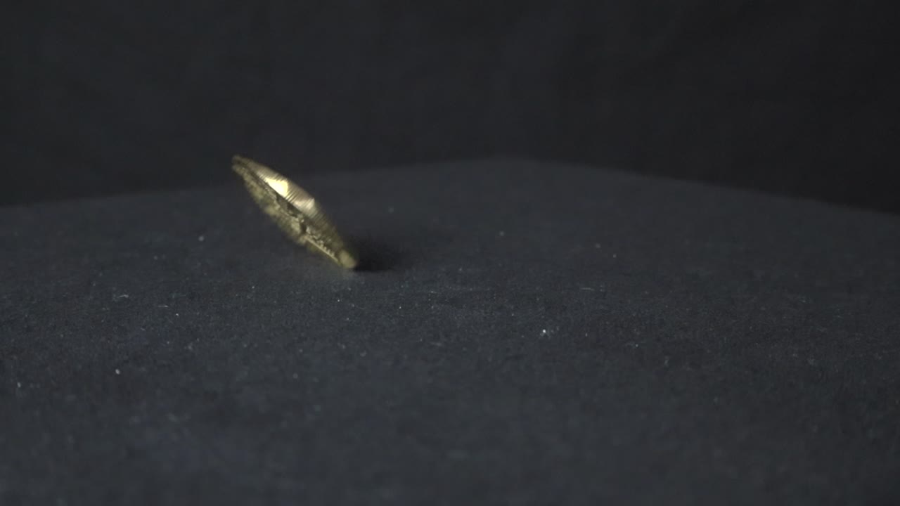 Bitcoin golden yellow cryptocurrency coin spinning in slow motion on a dark background and table creating reflections and shadows on the dark surface underneath. The coin spinning and eventually drops
