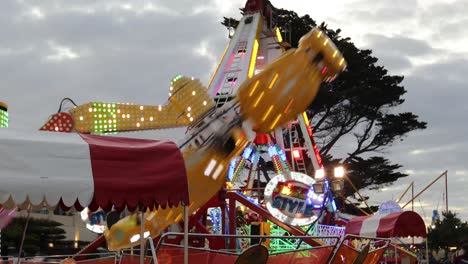 Carnival-Rides-spinning-and-rotating-with-flashing-neon-lights-at-dusk-background-cloudy-sky