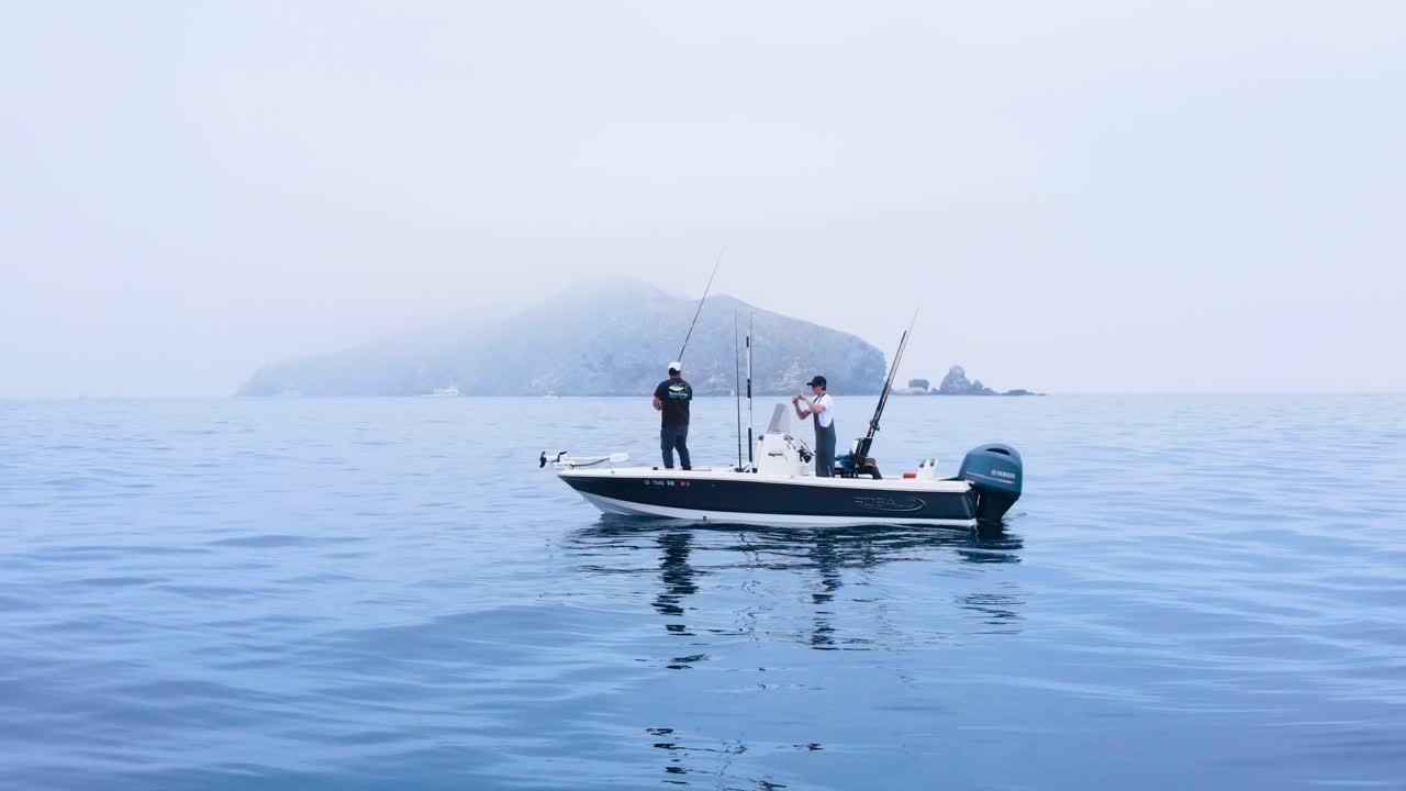 Aerial pullback dolly zoom from fishing boat in the calm waters near Coronado Islands, Mexico, with rugged cliffs in view as seagull chases out into air