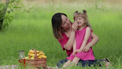 Family-weekend-at-picnic.-Daughter-child-girl-with-mother-on-grass-meadow-eating-merry,-cherry