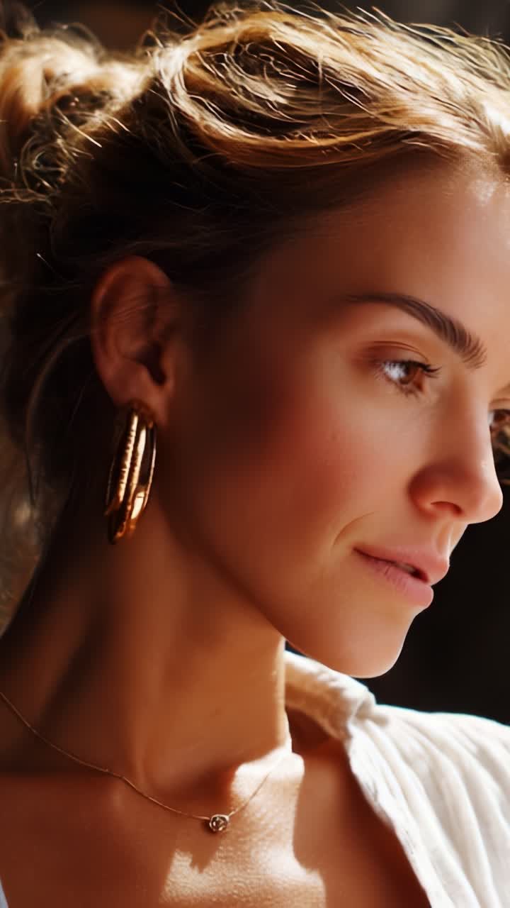 Primo piano accattivante di una donna con eleganti orecchini a cerchio e gioielli minimalisti, che emana bellezza naturale e irradia una luce calda e soffusa in un ambiente sereno
