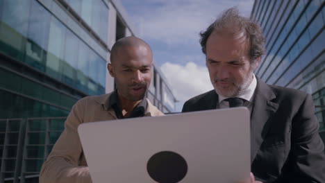 hombres de negocios confiados discutiendo proyectos con computadoras portátiles al aire libre