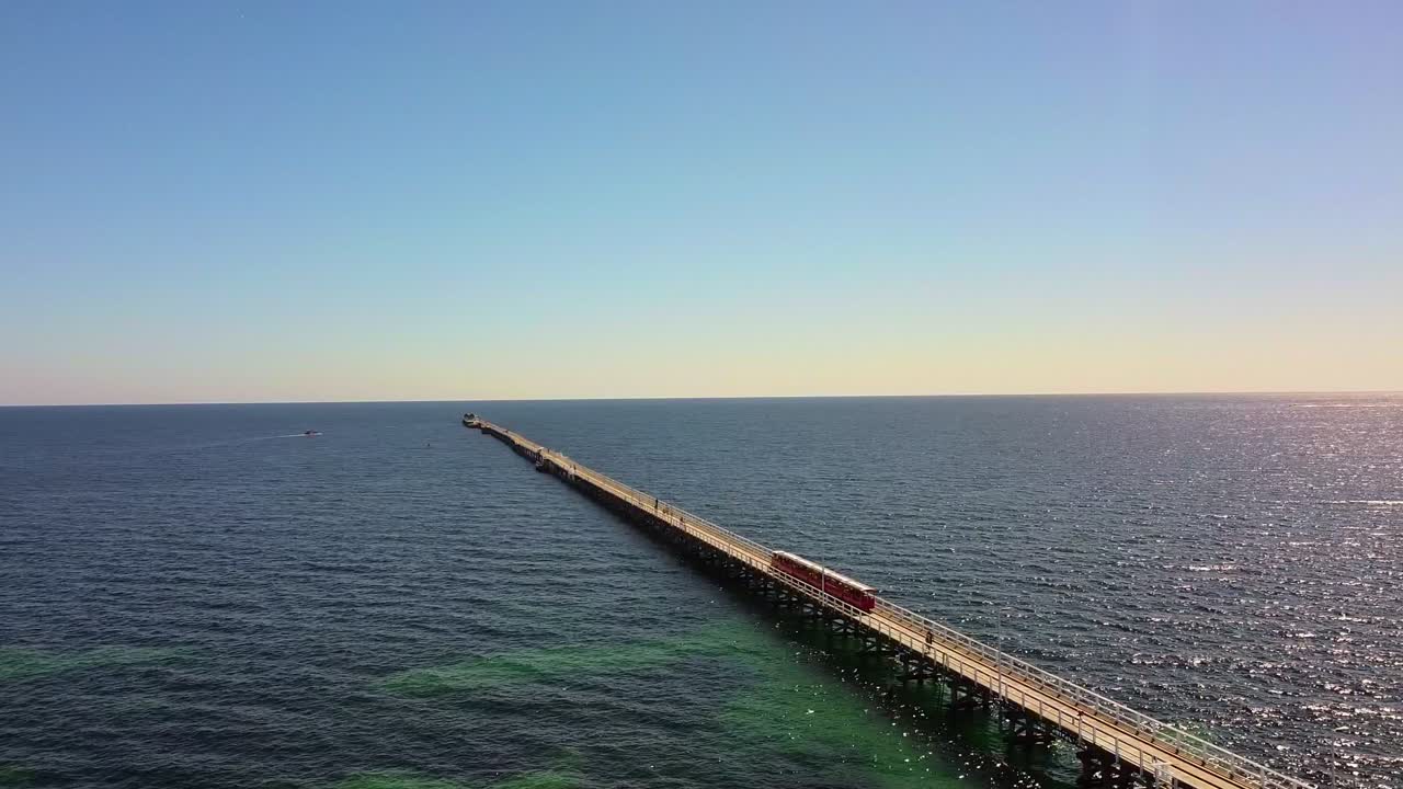 Aerial View of a Red Tram on a Long Pier Extending into the Ocean