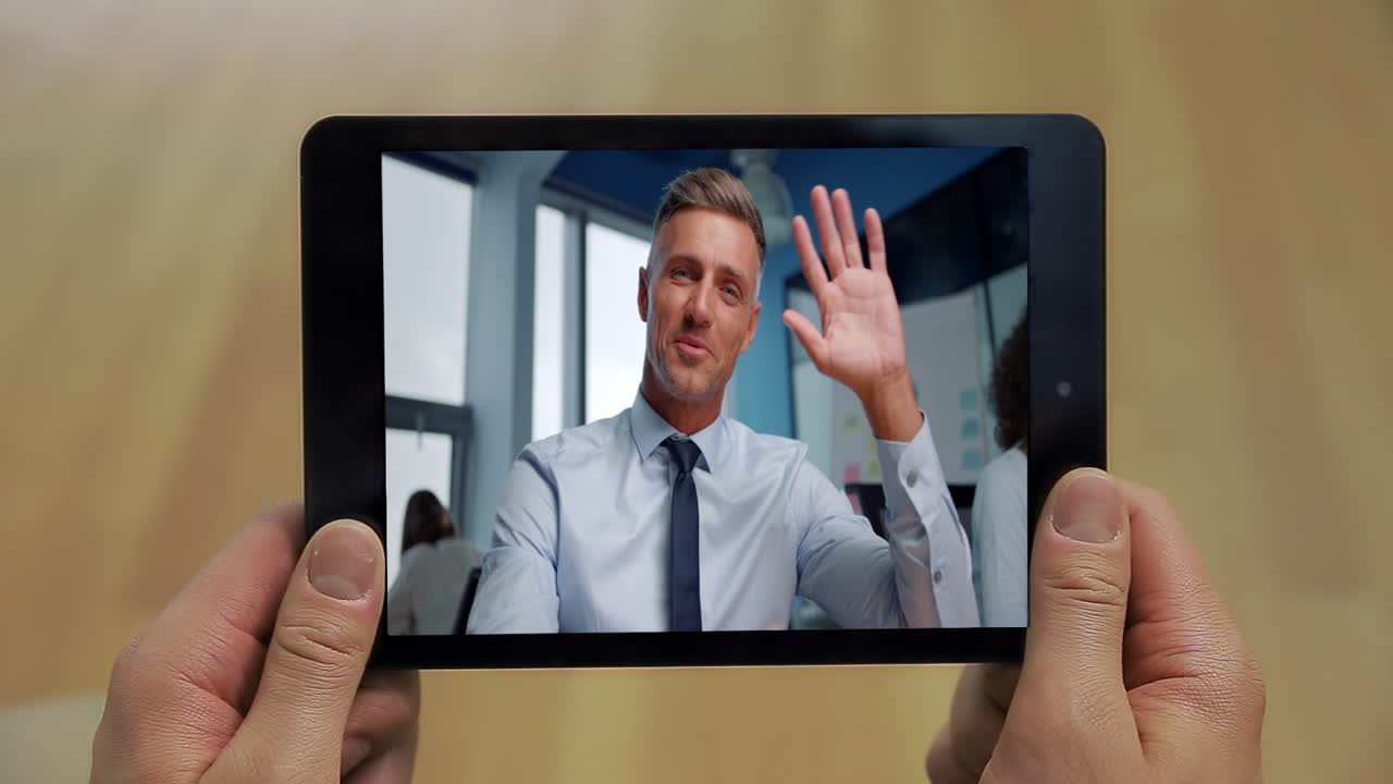 Etäinen esimies heiluttaa tabletin näyttöä toimistopuhelun lähikuvassa. Miehen kädet pitävät tablettia