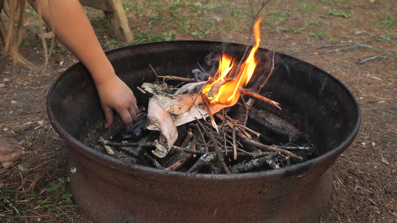 niño alimentando ramitas a una pequeña fogata