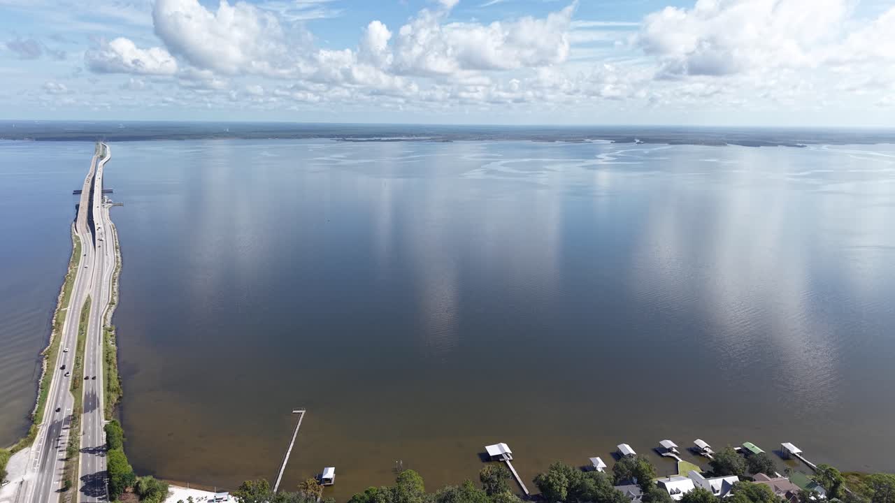 Tilted up drone fly near long Hwy 331 bridge crossing reflected water of Choctawhatchee Bay with boat docks, 30A, Florida, USA