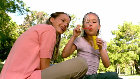 little girl blowing bubbles with her happy mother in the park