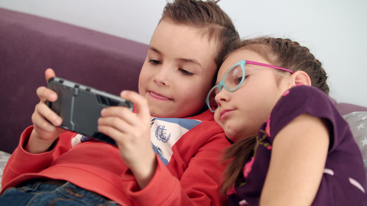niños usando teléfonos móviles en casa. hermana mirando el teléfono inteligente en las manos del niño