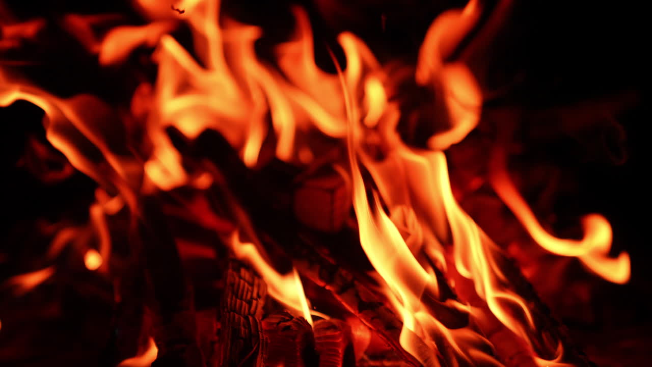 Small fire flames on the logs of wood. Comforting view of bonfire burning at night. Close up.