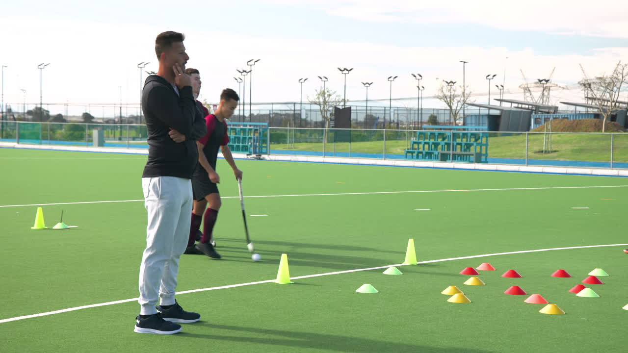 Coach observing male hockey players practicing drills on field with cones
