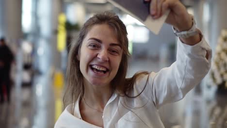 portrait of happy, beautiful american woman showing passport with flight tickets and waving it. looking and smiling to the