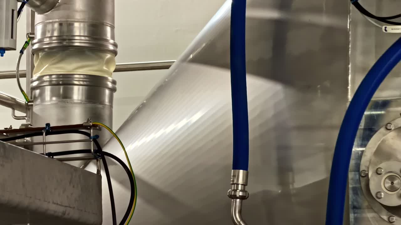 Blue hoses hang alongside stainless steel ducts in a factory environment. Useful for illustrating industrial processes or facility equipment layouts