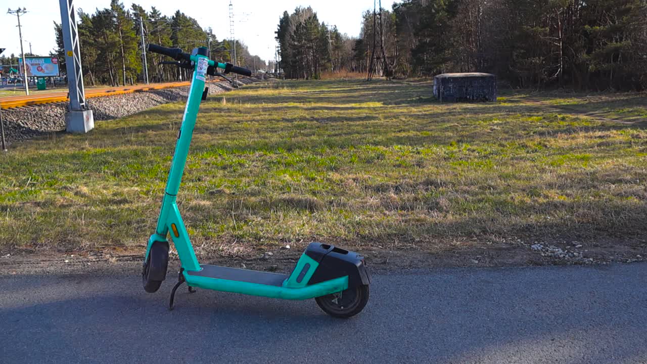 Greenish rental electric scooter parked on an asphalt path near a railway on a sunny day. Micromobility sharing services represent an eco friendly transport alternative for modern urban life