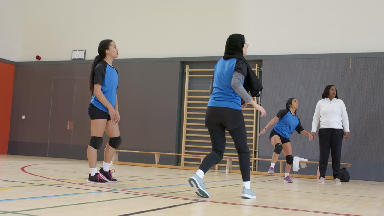 Equipe de vôlei feminina diversa praticando exercício de levantamento e ataque na academia com o treinador rolando a bola