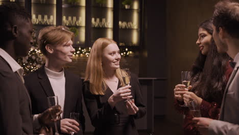 group friends wearing stylish clothes while talking and holding champagne glasses at new year's party