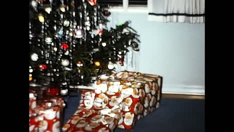 small christmas tree in front of window. circa usa - 1970s: a small christmas tree adorned with ornaments and lights placed in front of a window in a 1970s usa setting.