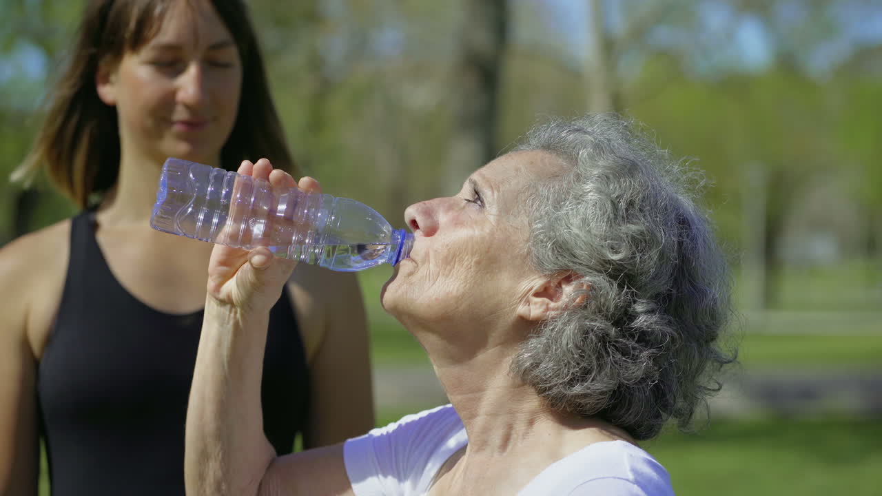 mujer mayor alegre bebiendo agua al aire libre.