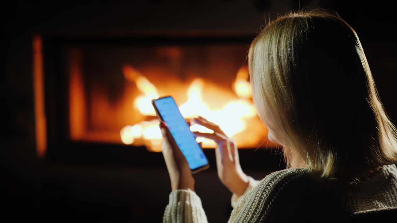 Una donna usa uno smartphone la sera seduta accanto al caminetto