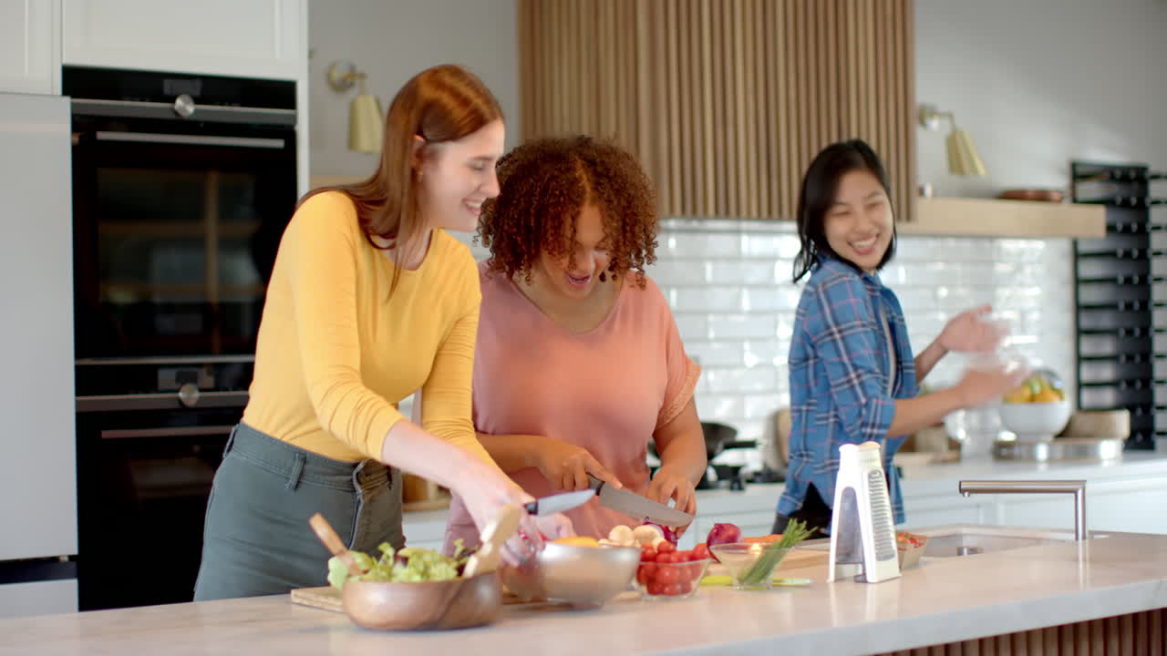Preparing meal, three women friends chopping vegetables and smiling in kitchen