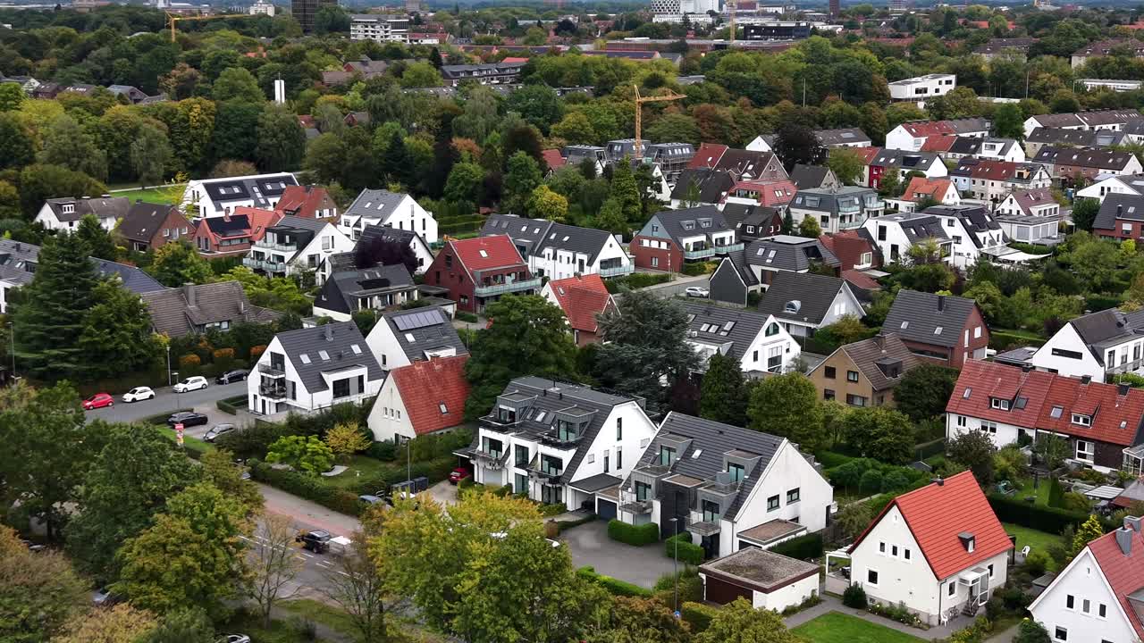 Drone flight over neighborhood with white hiouses and grey or orange roof tiles. Colored trees in fall season. Noble district of German town. Wide shot. Solar panels on rooftop producing green energy