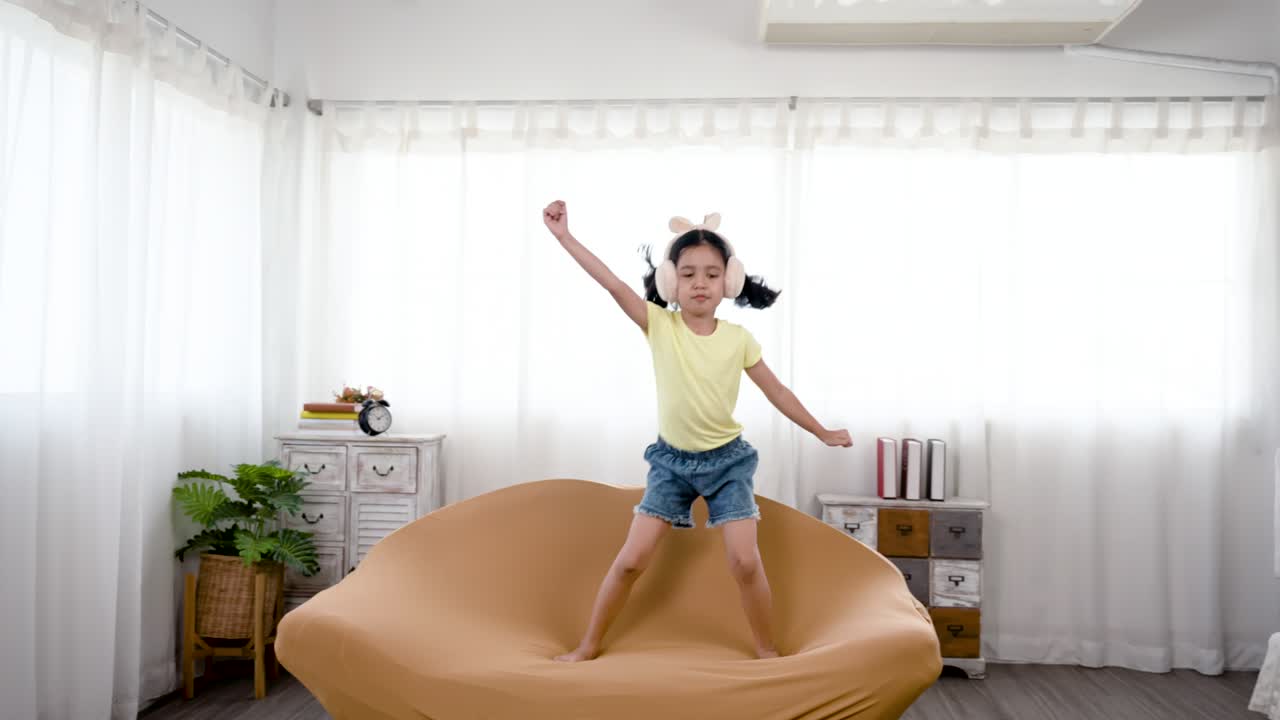 4k 50fps, 아시아 토끼 귀를 입은 귀여운 작은 소녀, 그녀의 침실에서 그녀의 좋아하는 소파에 뛰어, 그녀의 얼굴에 기쁜 표정.