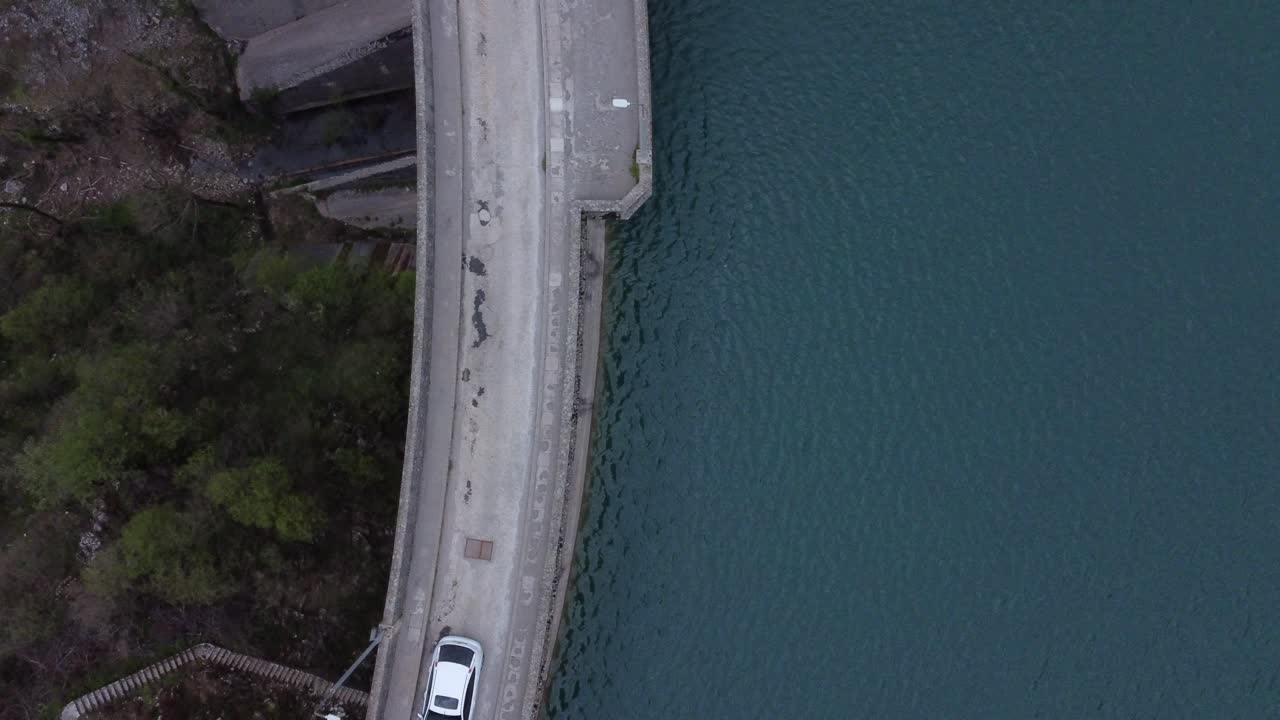 Top view shot of a hydroelectric dam and the nearby lake . White cars driving over the dam | 4K