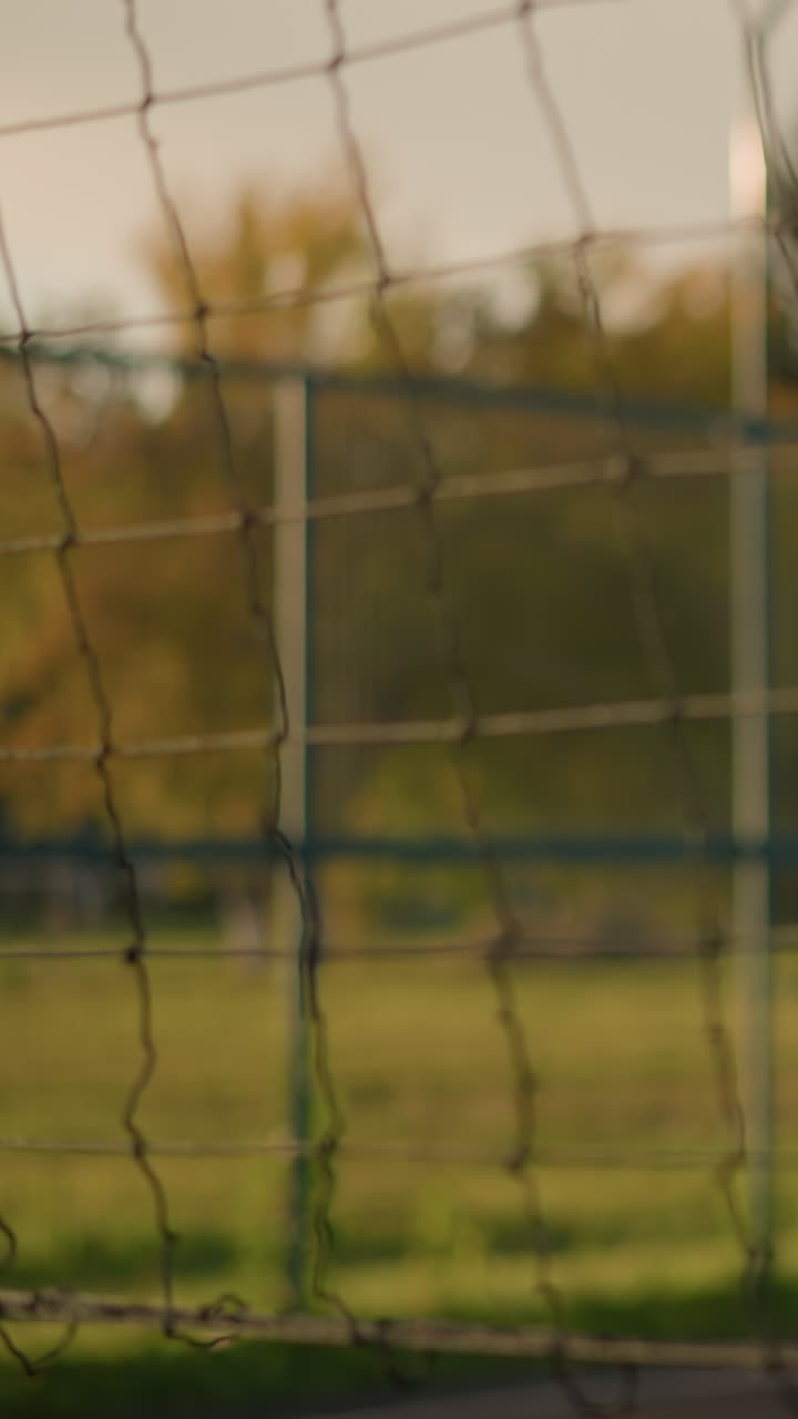 молодая леди играет в волейбол на открытом воздухе, корректируя свое положение возле волейбольной сетки, с размытым фоном с зелениной и зданиями на расстоянии, освещенными солнечным светом