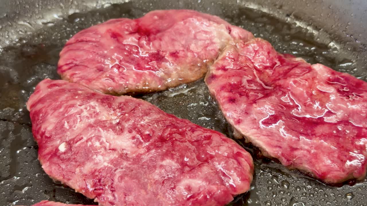 Bistecche di manzo marmorizzate crude sfrigolano e rosolano in una padella calda con olio bollente