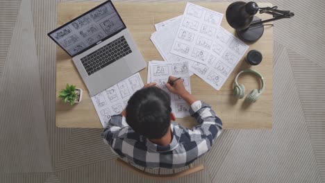 Top View Of Asian Male Artist Having A Backache While Drawing Storyboard For The Film On The Table With A Laptop And Headphones In The Studio