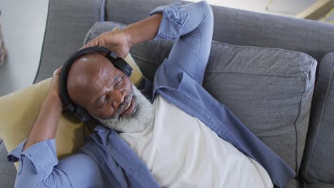 relaxed senior african american man in living room lying on sofa, wearing headphones