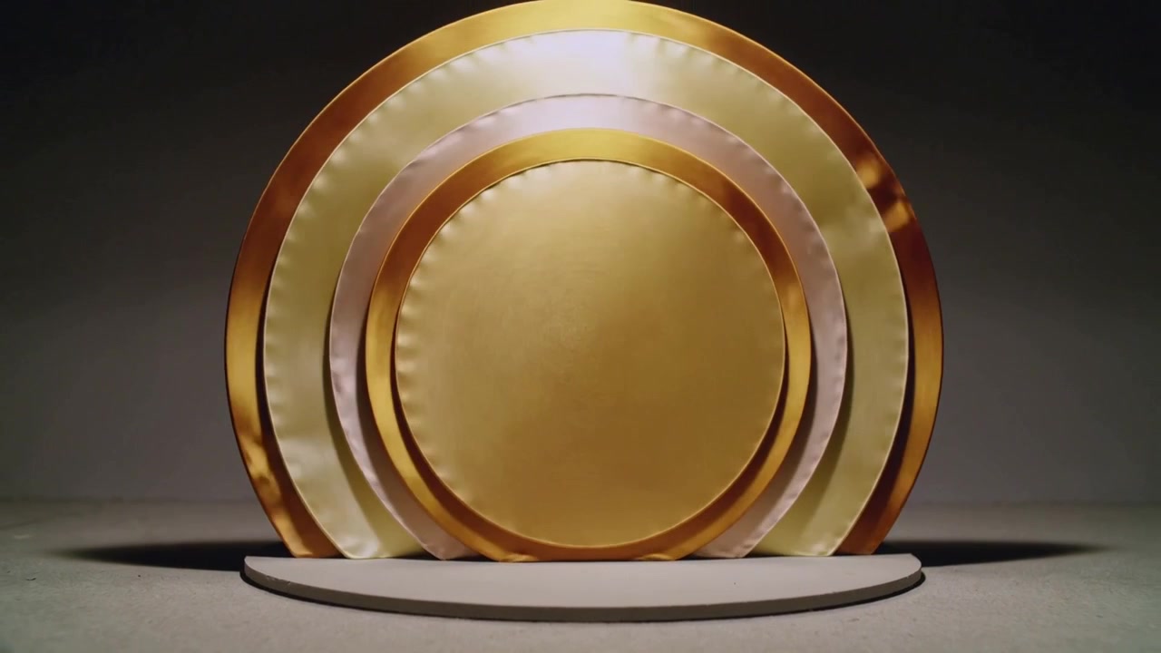 De spotlight verschuift, terwijl in elkaar passende panelen op een lage standaard draaien en een koperen rand en gouden glinsteringen aan de binnenkant onthullen.