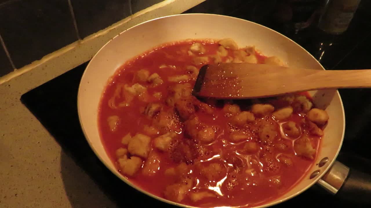 Adding red tomatoe sauce in the frying pan with chicken for preparing a recipe